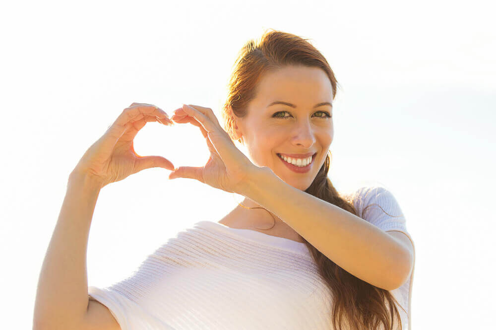 Woman outdoors with hands in heart shape.